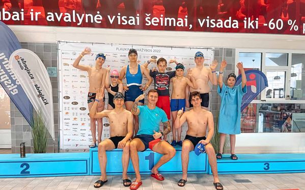 Plaukimo komanda su treneriu ant apdovanojimų pakylos