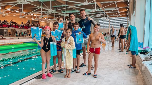 Vaikai su diplomais ir medaliais prie baseino po plaukimo varžybų